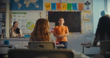 STEM Yenilenebilir Enerji Sınıfı: İlkokul öğrencisini kurula çağıran kadın öğretmen. Yetenekli çocuk, çeşitli çocuklarla dolu sınıfın önünde ekoloji ödevini sunar. Sınıf arkadaşları..