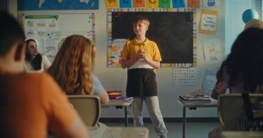 STEM Yenilenebilir Enerji Sınıfı: İlkokul öğrencisini kurula çağıran kadın öğretmen. Yetenekli çocuk, çeşitli çocuklarla dolu sınıfın önünde ekoloji ödevini sunar. Sınıf arkadaşları..