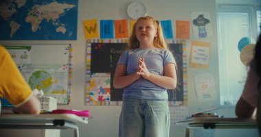 İlkokul öğrencisi utangaç kız sınıf ve öğretmenin önünde ekoloji bilgisi gösteriyor. Modern Sınıfta Çevre Bilimi Dersi sırasında Masalarda oturan Zeki Çocuklar. BTMM Eğitim. Yavaş Hareket.