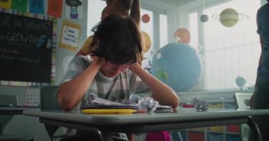 Agresif sınıf arkadaşları onu taciz ederken, kağıtları fırlatırken ve gülerken sınıfın masasında tek başına oturan ilkokul çocuğu. Okul zorbalığı, Akran Tacizi ve Toksik Okul Ortamı.