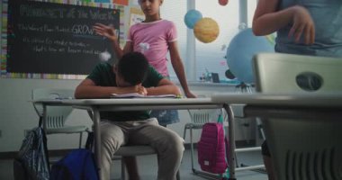 Üzgün Afro-Amerikan İlköğretim Okulu öğrencisi, sınıf arkadaşları ona zorbalık yaparken, gülerken ve kağıt fırlatırken tek başına masada oturuyor ve ağlıyor. Okulun zorbalığından ve ırksal tacizden muzdarip.