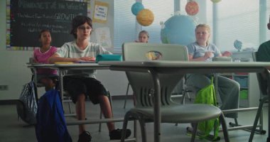 Depresyondaki ilkokul çocuğu sınıfın masasında tek başına otururken agresif sınıf arkadaşları onu taciz ediyor, kağıtları fırlatıyor ve gülüyor. Okul zorbalığı, Akran Tacizi ve Toksik Okul Ortamı.