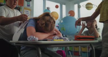 İlkokul öğrencisinin yalnız başına masasında oturması ve sınıf arkadaşları ona zorbalık yaparken ağlaması, gülmesi ve kağıtları fırlatması. Okul zorbalığından, arkadaş tacizinden ve duygusal tacizden muzdarip kız.