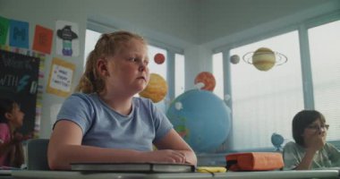 Agresif sınıf arkadaşları onu taciz ederken, Kağıtları fırlatırken ve gülerken, Sınıfta Tek Başına Oturan İlkokul Kızları. Okul zorbalığı, Akran Tacizi ve Toksik Okul Ortamı.