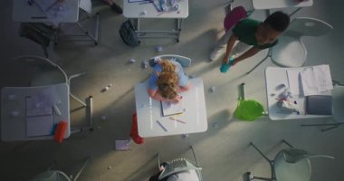 Stresli İlköğretim Okulu Kızı Masada Oturuyor, Agresif Sınıf Arkadaşları Onu Taciz Ederken Kameraya Bakıyor, Kağıt Fırlatıyor ve Gülüyorlar. Okul zorbalığı ve Toksik Okul Ortamı. Üst Görünüm Döndürülüyor.