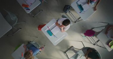 Depresyondaki ilkokul çocuğu sınıfın masasında tek başına otururken agresif sınıf arkadaşları onu taciz ediyor, kağıtları fırlatıyor ve gülüyor. Okul zorbalığı ve Toksik Okul Ortamı. Üst Görünüm Döndürülüyor.