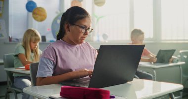 Bilgisayar Bilimi Dersi: İlkokul öğrencisi kız masamda oturuyor, sınıfta dizüstü bilgisayar kullanıyor. Temel Programlama Dillerini Öğrenen Erkekler ve Kızlar Grubu ve Dijital Tabletler ve Dizüstü bilgisayarlarda İnternet Güvenliği.