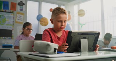 Bilgisayar Bilimi Dersi: İlkokul çocuğu masada oturuyor, Sınıfta Tablet Bilgisayar kullanıyor. Temel Programlama Dili ve İnternet Güvenliğini Dijital Aygıtlarda Öğrenen Kız ve Erkekler Grubu.