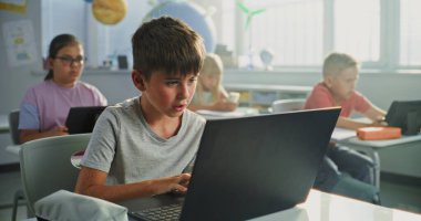 İlkokul çocuğu masada oturuyor, sınıfta dizüstü bilgisayar kullanıyordu. Bilgisayarları ve Tablet Bilgisayarları üzerinde çalışan, Bilgisayar Bilimi, Temel Programlama ve Kodlama okuyan Zeki Çeşitli Çocuklar Takımı.