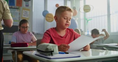 Modern Sınıfta Masalarda Oturan İlkokul çocuklarına Okul Sınavı Sonuçları Veren Öğretmenler. Coğrafya veya Fen Bilimleri Sınavı 'nda Harika Notlar Aldı ve Kutladı.