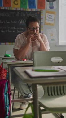 Sınıfta masa başında oturan yorgun bayan öğretmen dersten sonra dinleniyor. Eğitim Ortamı 'nda Kadın Stres, Burnout ve Zihinsel Yorgunluk İlkokulda Çalışıyor. Dikey Çekim.