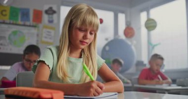 İlköğretim Okulu Kızı Masa başında oturuyor, Okul Defterinde Yazma Görevleri yapıyor. Coğrafya Dersinde Ders Veren, Modern Renkli Sınıfta Bilim Çalışan Zeki Çeşitli Çocuklar Takımı.