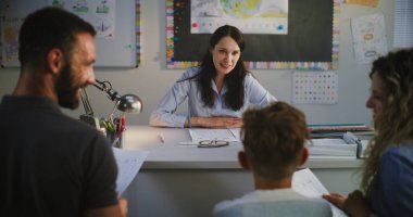 Anne ve babasına ilkokul öğrencisinin okul sınavı sonuçlarını veren bayan öğretmen. Ailesiyle Akademik İlerleme ve Öğrenci Notları Hakkında Konuşan Öğretmen. Çocuk Gelişimini Desteklemek İçin Toplantı.