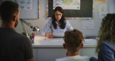 İlköğretim Okulu Öğrencisinin Ailesine Sınav Sonuçları Veren Bayan Öğretmen. Yetersiz Performans, Düşük Notlar ve Öğrenci Davranışı Hakkında Konuşan Öğretmen. Ebeveynler Öğrenen Çocukları Desteklemek İçin Akşam Vakti.
