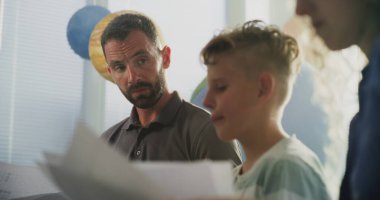 Oğullarının Sınav Notlarına Sınıfta Bakan Ebeveynler. İlkokul öğrencisinin kötü okul performansı yüzünden aileler üzgün. Çocukların Gelişmesini Desteklemek İçin Toplantı. Ağır çekim. Kapat..