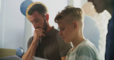 Oğullarının Sınav Notlarına Sınıfta Bakan Ebeveynler. İlkokul öğrencisinin kötü okul performansı yüzünden aileler üzgün. Çocukların Gelişmesini Desteklemek İçin Toplantı. Ağır çekim. Kapat..