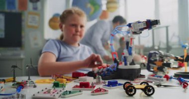 Masada oturan yetenekli genç kız, Robotik Kol Modeli okuyor. Modern Sınıfta İlkokul Öğrenim Mühendisliği, Bilim ve Robot Teknolojisi. Yaratıcı Etkinlik, BTMM Eğitimi