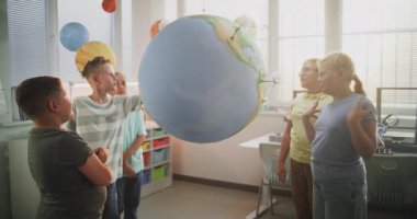 Ekoloji BTMM Sınıfı: İlkokul öğrencileri konuşuyor, rüzgar türbinlerinin minyatür modellerine ve Dünya 'daki güneş panellerine bakıyor. Akıllı Çocuklar Bilim okuyor, Yenilenebilir Enerji Toprak Gezegeni Modelini Kullanıyor.