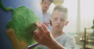 Ekoloji BTMM Sınıfı: İlkokul çocuğu Dünya 'ya Rüzgâr Türbininin Minyatür Modelini Ekliyor. Modern Sınıfta Zeki Genç Öğrencilere Bilim ve Yenilenebilir Enerji Kaynaklarını Açıklayan Erkek Öğretmenler.