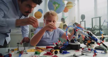 Masada oturan yetenekli genç kız, Erkek Öğretmenle Robotik Kol Modeli okuyor. Modern Sınıfta İlkokul Öğrenim Mühendisliği, Bilim ve Robot Teknolojisi. STEM Eğitimi.