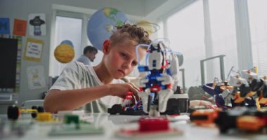 Masada oturan yetenekli genç çocuk, Robotik Kol Modeli okuyor. Modern Sınıfta İlkokul Öğrenim Mühendisliği, Bilim ve Robot Teknolojisi. Yaratıcı Etkinlik, BTMM Eğitimi.