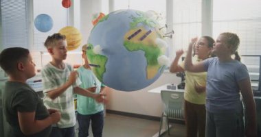 Çevre Bilimi Dersi: İlkokul çocukları Dünya Modeline Minyatür Rüzgar Türbinleri ve Güneş Panelleri Ekliyorlar. Sınıfta Yenilenebilir Enerji Kaynakları Öğrenen Yetenekli Çocuklar. STEM Eğitimi.