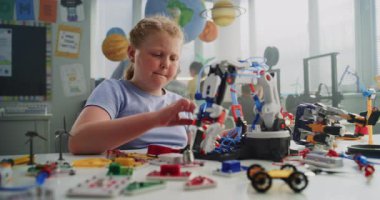 Masada oturan ilkokul öğrencisi kız, Yenilikçi Robot Kollar Modeli okuyor. Zeki genç öğrenciye yardım eden öğretmen. Bilim, Mühendislik ve İleri Teknoloji Dersi. Etkileşimli BTMM Sınıfı.