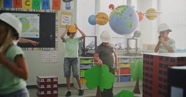 Hardhat 'lı Akıllı Genç Çocuklar Büyük Mukavva Şehir Modelleri, Yollar, Ağaçlar ile Etkileşimli Şehir Planlaması Yapıyor. BTMM etkinliğinde ilkokul çocuklarına rehberlik eden bayan öğretmen. Doli Vuruşu.