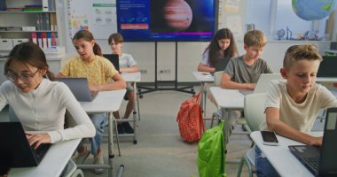 İlkokul çocukları dizüstü bilgisayar kullanıyor, sınıfta dijital sanat dersi sırasında yaratıcı görevler yapıyor. Resim Oluşturmak için Yapay Zeka Yazılımını Gösteren Dijital Ekran. Etkileşimli BTMM Eğitimi. Doli Vuruşu.