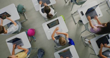 İlkokul öğrencileri dizüstü bilgisayarlarda yaratıcı projeler üzerinde çalışıyor, Sanat sınıfında dijital beceriler geliştiriyor. Dijital cihazlarda resim çizen, resim yapan küçük çocuklar. İnteraktif STEM Öğrenme. Üst Görünüm.