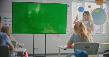 Modern Sınıfta İlkokul Öğrencilerini Eğiten Bayan Öğretmen. Büyük Dijital Ekran ve Krom Anahtar. Eğitim İçeriği veya Etkileşimli Görsel Efektler için Yeşil Ekran Şablonu