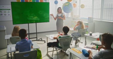 Sınıfta İlkokul Öğrencilerini Eğiten Bayan Öğretmenler. Büyük Dijital Ekran ve Krom Anahtar. Eğitim İçeriği veya Etkileşimli Görseller için Yeşil Ekran Şablonu. Doli Vuruşu.