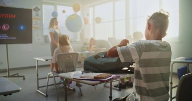 İlkokul öğrencileri sınıfa hazırlanıyor, okul malzemelerini modern sınıftaki masalara diziyor. Astronomi Dersinin Başında Çeşitli Çocuklar Kadın Öğretmenler Grubu. Yavaş Hareket