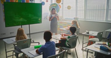 Modern Sınıflar: Chromakey Mockup ile Büyük Dijital Ekran kullanarak İlkokul Çocuklarına Öğretmenlik Yapan Kadın Sınıfı. Eğitim İçeriği veya Etkileşimli Görseller için Yeşil Ekran Yer Tutucu. Doli Vuruşu.