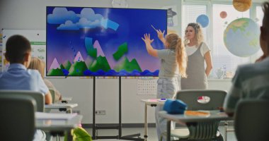 Coğrafya Sınıfı: Dijital Ekran Kullanarak İlkokul Çocuklarına Öğretmenlik Yapan Kadın Öğretmenler. Genç Kız, Sınıf Arkadaşlarının Önünde Su Döngüsü ve Hava Durumu Faktörlerini Açıklıyor, Sorulara Cevap Veriyor.