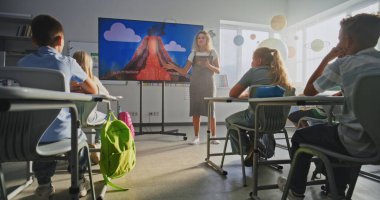 Jeoloji sınıfı: Tablet Bilgisayarlı Kadın Öğretmen İlkokul Çocuklarına Dijital Ekran Kullanarak Öğretiyor. Volkan ve Coğrafya 'da Oturan ve Öğrenen Genç Öğrenciler Grubu. Doli Vuruşu