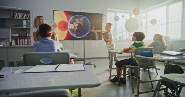 Tablet Bilgisayarlı İlkokul Çocuğu Sınıf Arkadaşları ve Öğretmen Dijital Ekran Kullanıyor 'da Güneş Sistemi ve Gezegenler Hakkında Sunum Yapıyor. Sınıfta Uzay Astronomisi okuyan Zeki Çocuklar.