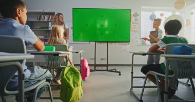 Tablet Bilgisayarlı İlkokul Çocuğu Sınıf Arkadaşlarının Önünde Bilgi Gösterme ve Öğretmen Chromakey Mockup ile Dijital Ekran Kullanıyor. Etkileşimli Görsel Efektler için Yeşil Ekran Yer Tutucu.