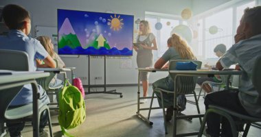 İlkokul öğrencileri hava durumu faktörleri hakkında temel bilgileri inceliyor. Coğrafya dersi alan çocuklara su döngülerini anlatan tablet bilgisayarlı bayan öğretmen dijital ekranı kullanıyor. Doli Vuruşu.