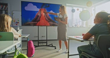 İlkokul öğrencileri Volkanik Patlama Süreci Hakkında Temel Bilgiler Çalışıyor. Akıllı çocuklara dijital ekranı kullanarak jeoloji ve bilimi açıklayan tablet bilgisayarlı bayan öğretmen. Doli Vuruşu