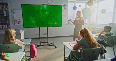 Modern Sınıfta İlköğretim Okulu Öğrencilerini Eğiten Tablet Bilgisayar Öğretmeni. Büyük Dijital Ekran ve Chroma Key Mock Up. Eğitim İçeriği için Yeşil Ekran Şablonu.