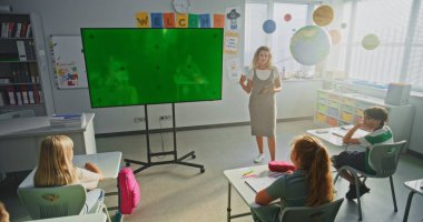 Modern Sınıfta İlköğretim Okulu Öğrencilerini Eğiten Tablet Bilgisayar Öğretmeni. Büyük Dijital Ekran ve Chroma Key Mock Up. Eğitim İçeriği için Yeşil Ekran Şablonu.