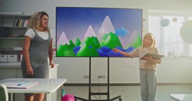 Tablet bilgisayarlı ilkokul kızı su döngülerini ve sınıf arkadaşlarının önündeki hava faktörlerini ve dijital ekranı kullanan öğretmeni açıklıyor. Modern Sınıfta Coğrafya Çalışan Akıllı Çocuklar.