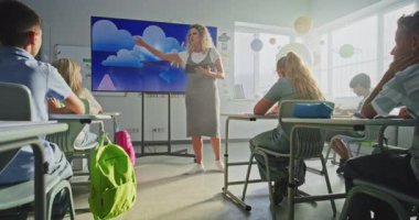 İlkokul öğrencileri hava durumu faktörleri hakkında temel bilgileri inceliyor. Coğrafya dersi alan çocuklara su döngülerini anlatan tablet bilgisayarlı bayan öğretmen dijital ekranı kullanıyor. Doli Vuruşu.