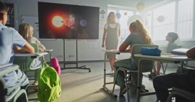 Astronomi sınıfı: Dijital Ekran kullanarak İlkokul çocuklarına Güneş Sistemi Açıklayan Kadın Öğretmen. Bir grup genç kız ve erkek el kaldırıyor, sınıfta uzay bilimi öğreniyorlar. Doli Vuruşu.