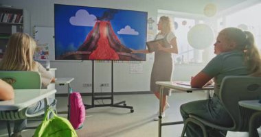 Jeoloji sınıfı: Tablet Bilgisayarlı Kadın Öğretmen İlkokul Çocuklarına Dijital Ekran Kullanarak Öğretiyor. Volkan ve Coğrafya 'da Oturan ve Öğrenen Genç Öğrenciler Grubu. Doli Vuruşu