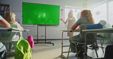 Tablet Bilgisayarlı Bayan Öğretmen İlkokul Öğrencilerini Sınıfta Eğitiyor. Büyük Dijital Ekran ve Krom Anahtar. Eğitim İçeriği için Yeşil Ekran Şablonu. Doli Vuruşu.