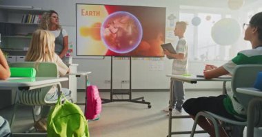 Tablet Bilgisayarlı İlkokul Çocuğu Sınıf Arkadaşları ve Öğretmen Dijital Ekran Kullanıyor 'da Güneş Sistemi ve Gezegenler Hakkında Sunum Yapıyor. Sınıfta Uzay Astronomisi okuyan Zeki Çocuklar.