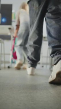 İlkokul çocuklarının sınıfa girerken, sırt çantalarını açarken ve okul malzemelerini masaya sererken diz üstü çekimleri. Bayan Öğretmen, oğlanları ve kızları selamlıyor. Ağır çekim. Dikey Çekim.