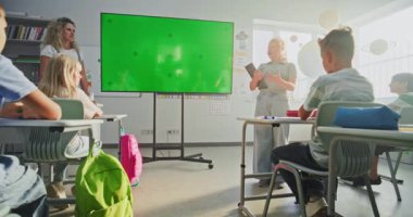 Tablet Bilgisayarlı İlkokul Kızı Sınıf Arkadaşlarının Önünde Bilgi Gösterme ve Öğretmen Chromakey Mockup ile Dijital Ekran Kullanıyor. Etkileşimli Görsel Efektler için Yeşil Ekran Yer Tutucu.